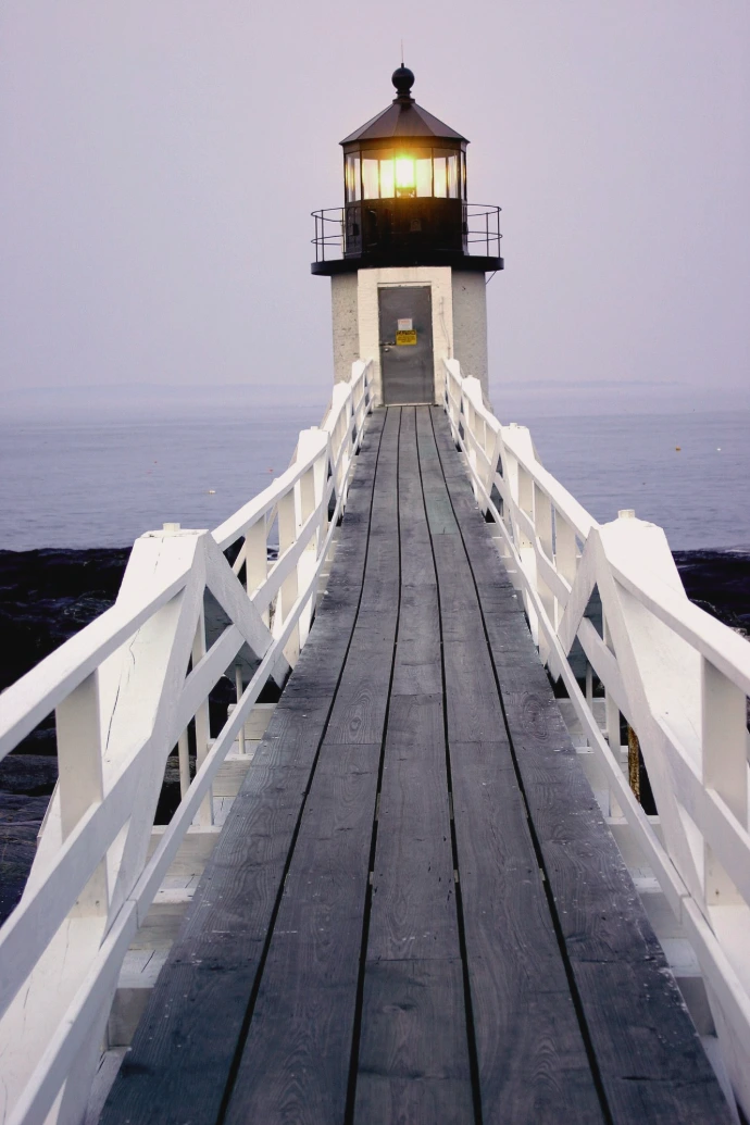 Wooden walkway leads to a lighthouse at dusk.